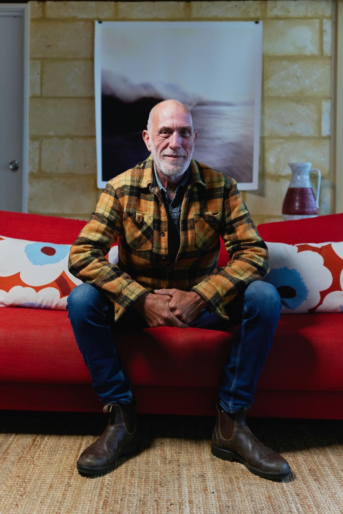 Portrait of Pete Hill, Director of SpatialCo, seated on a red sofa in front of one of his coastal prints